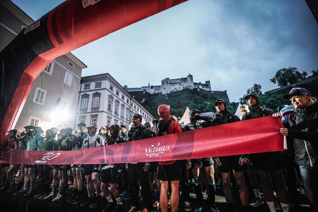 Runners under the red start arch at the Mozart 100 in Salzburg, in heavy rain before dawn.